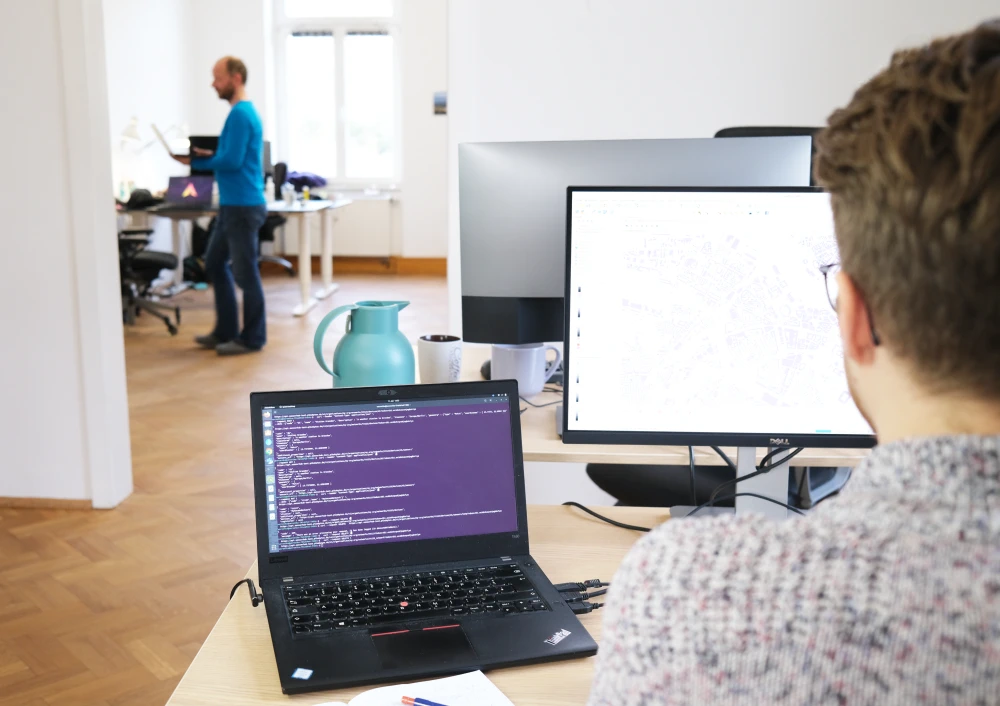 Blick über die Schulter eines Mitarbeiters in einen hellen Büroraum.