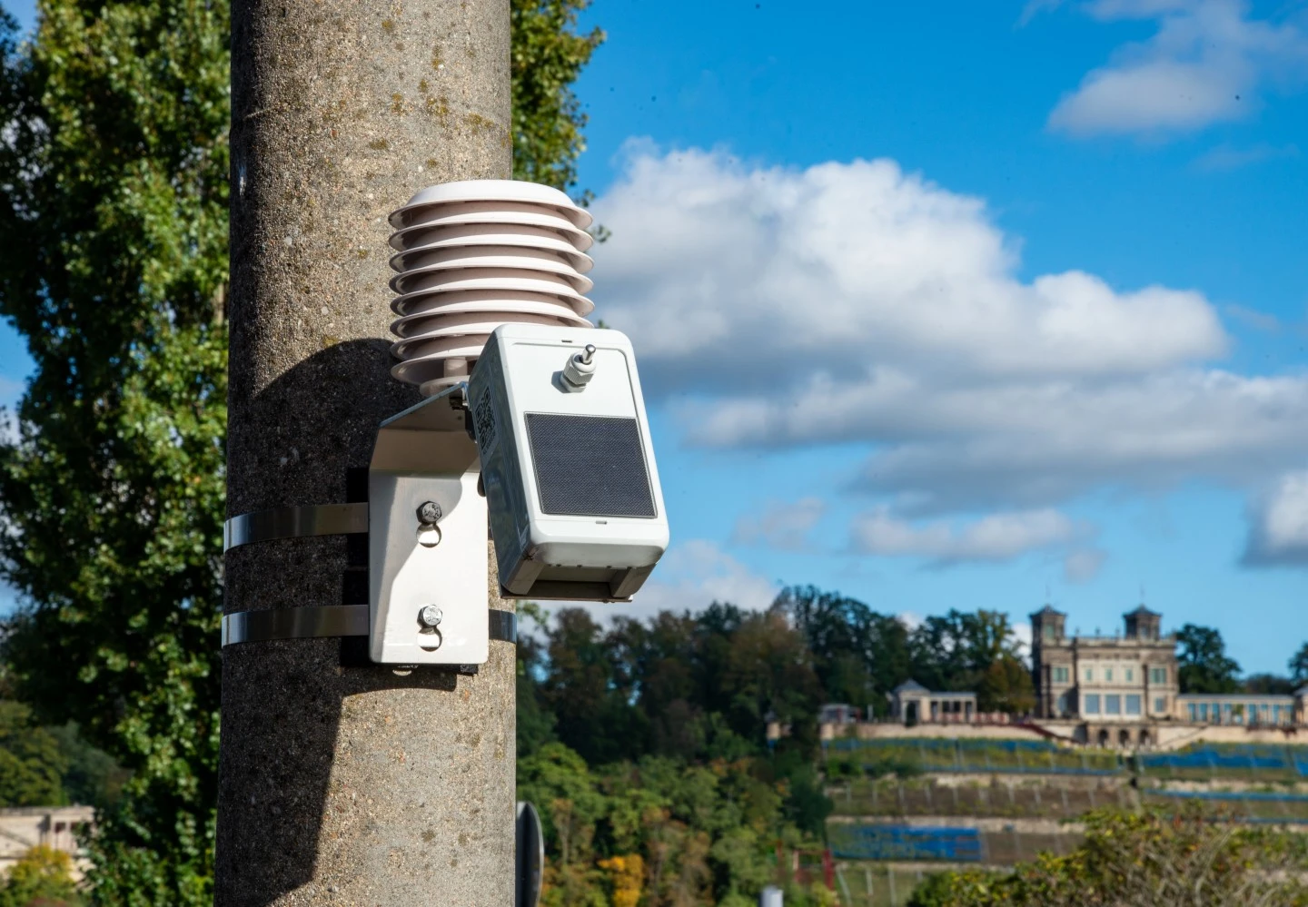 A climate sensor is attached to a lamppost. In the background, you can see the slopes of the Elbe River and a mansion.
